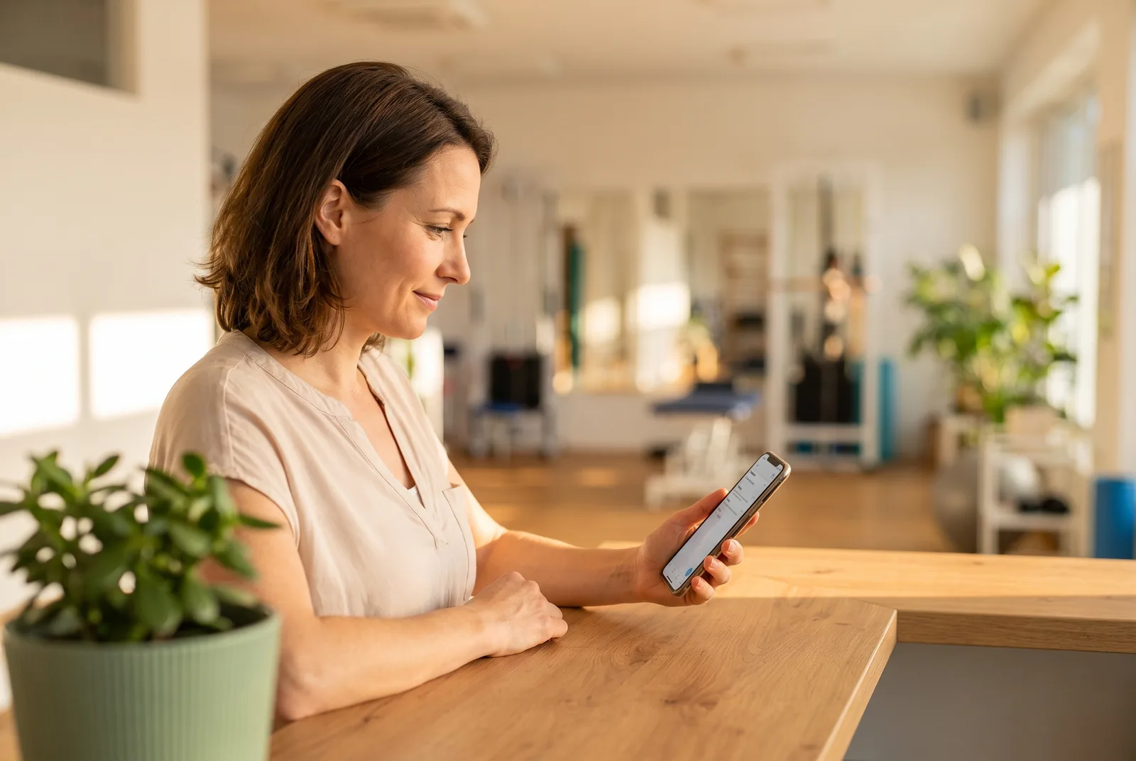 Inhaberin einer Physiotherapiepraxis liest am Empfang eine Nachricht auf ihrem Smartphone